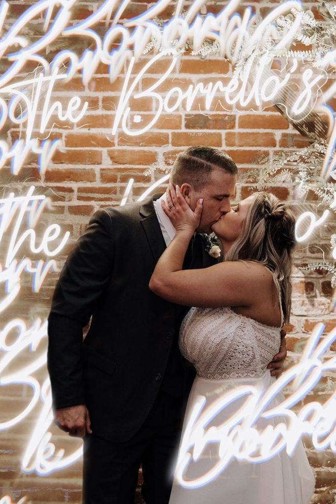 bride and groom kissing under a neon sign