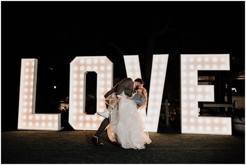 bride and groom kissing with light up love sign