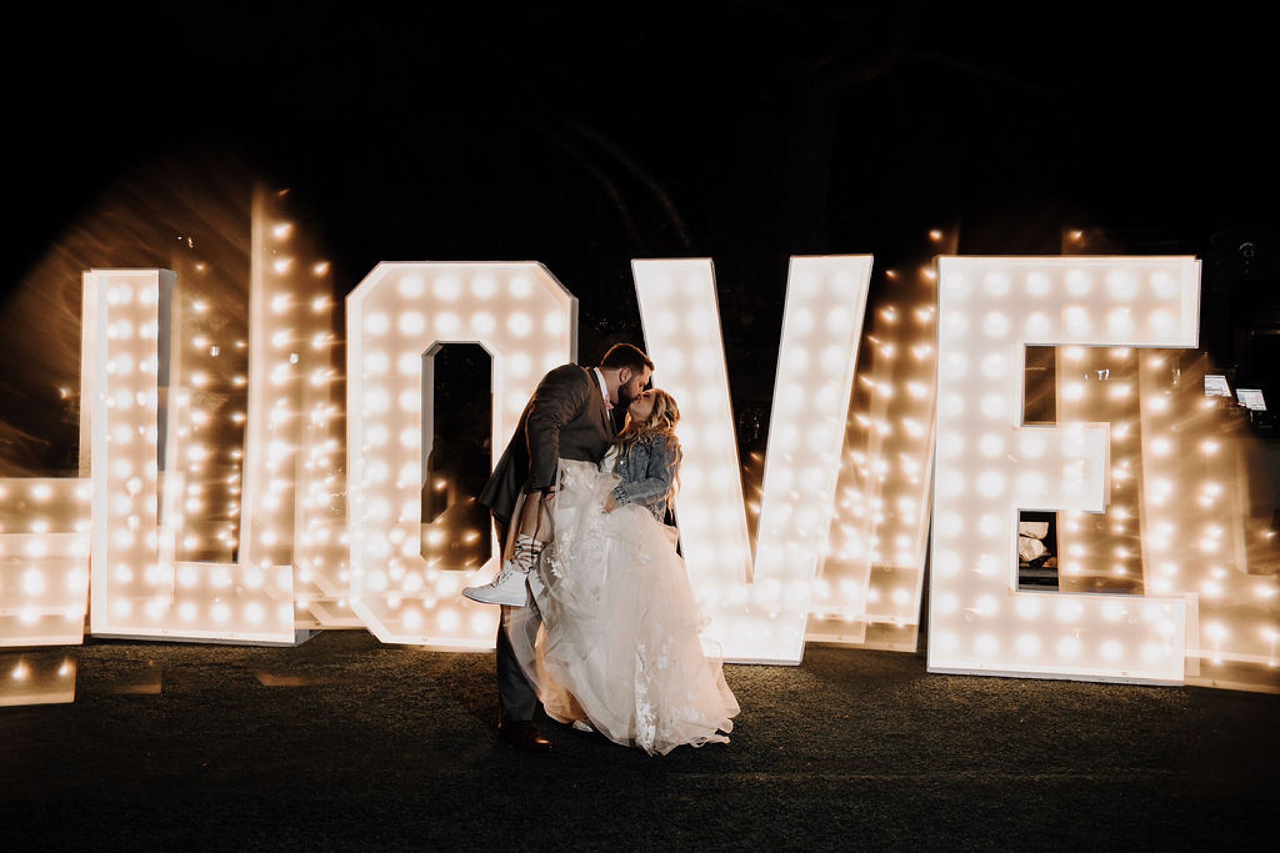 couple kissing in front of love marquee sign